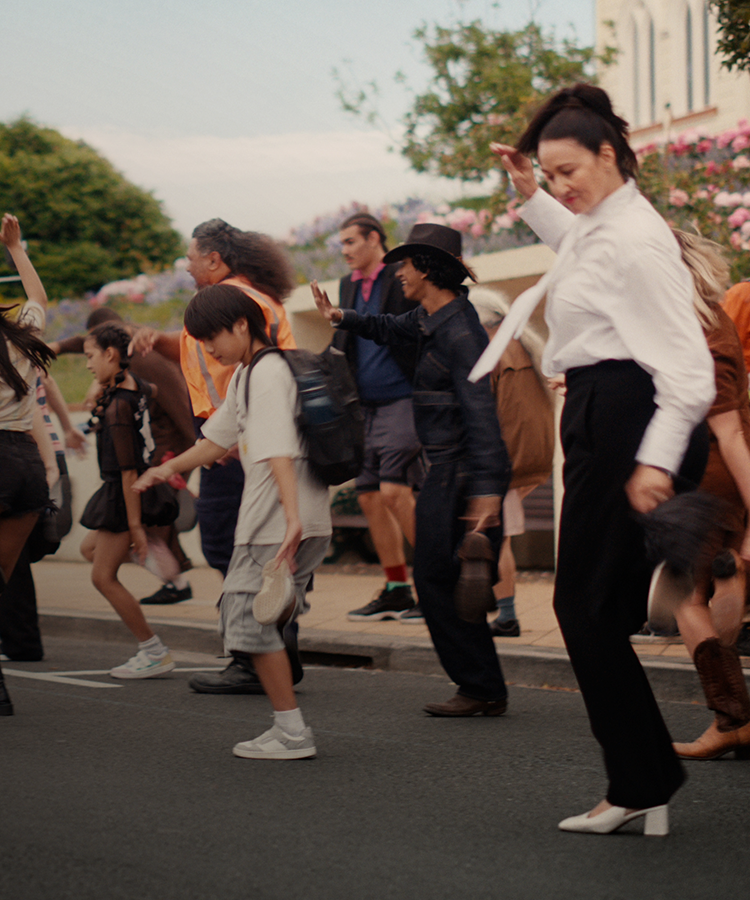 A large group of happy people dancing in the street. A bus with the words "Feel Good" in the background.