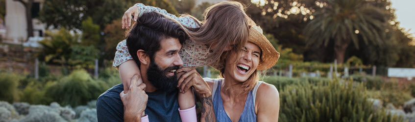 A young couple together with their daughter who is sat on her dad's shoulders